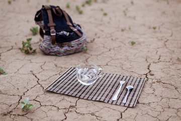 A cup of water and cutlery on the dried ground. The concept of water, as the most necessary for human survival.