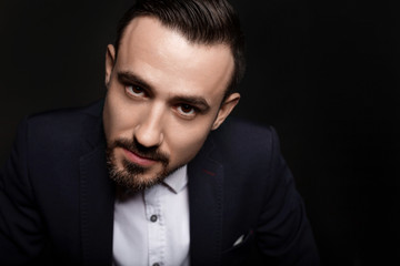 Handsome man attentively looking. Bearded guy in a blue jacket and white shirt. Black background.