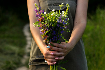 A young woman with a bouquet of wild flowers (chamomile, lupine, clover) in her hands is standing in a meadow, close-up. Summer, background, concept
