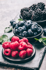 Fresh berries with raspberries, blueberries, blackberries in bowl on a stone stand on a dark metal background.