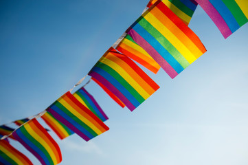 Celebratory gay pride rainbow flag bunting fluttering backlit by the sun against clear blue sky copy space