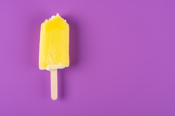 yellow popsicle with couple of bites on a purple background