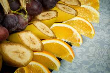 Fototapeta na wymiar closeup sliced bananas, oranges and grapes on big plate