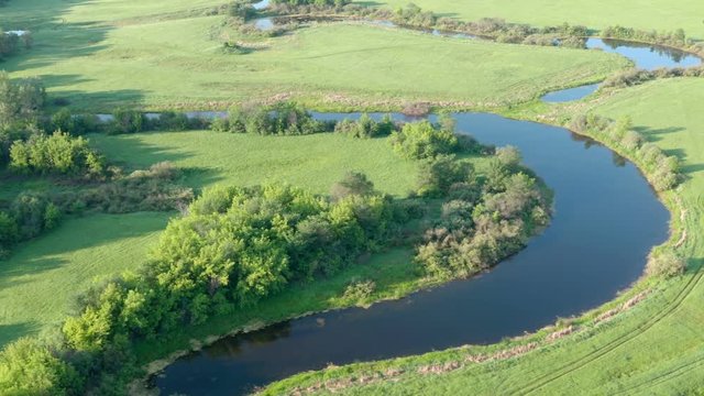 Aerial high angle lateral shot along lakes and trees.Along river, meadows and green fields.Tall brich trees. Summer day, morning.