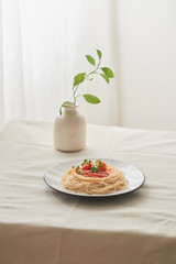 Food, spaghetti bolognese sauce in white dish and a vase of plants on a white prepared table