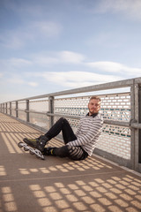 one young man, posing on a bridge, wearing inline skates.
