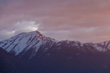 Naklejka na ściany i meble Snowy mountain with stormy red sunset sky