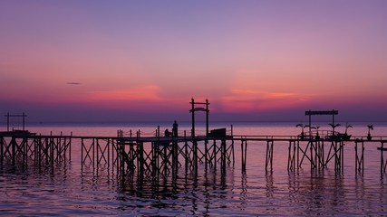 Two silhoutte people on the bridge on the beach at sunset with a purple sky