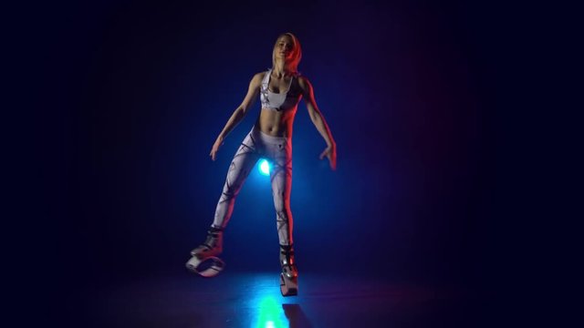 Pretty woman in sports suit doing exercises in kangoo jumps.