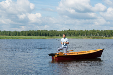 Fototapeta na wymiar a man stands in a wooden boat in the middle of the lake and fishing for spinning