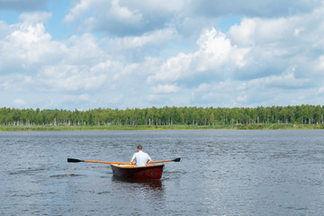 man rowing in a wooden boat, floating on a lake on a sunny day, active weekend, rear view