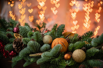 Christmas mood. Beautiful festive arrangement of fresh spruce in a rustic wooden box. Bokeh hearts of Garland lights on background. Decorated with slices orange, gold balls , cones