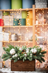 Christmas mood. Beautiful festive arrangement of fresh spruce in a rustic wooden box. Bokeh hearts of Garland lights on background. Decorated with Bells, balls silver, white cotton and cinnamon