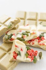 Handmade chocolates bar. White chocolate bar with pistachio nuts and dried fruit cherries. Copy space. Light key on white Desk