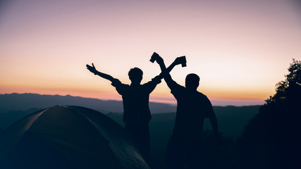 Happy time of two hiker man holding coffee cup near camping tent on mountains at sunset background. travel concept.