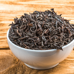 Dried tea is poured into a ceramic cup on a wooden plank table.