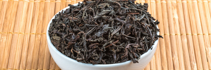 Dried tea is poured into a ceramic cup on a bamboo mat.