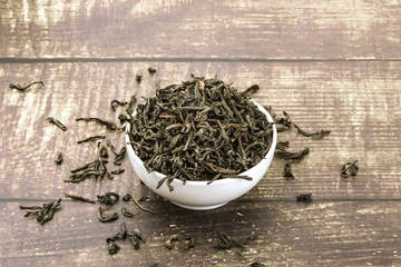 Dried tea is poured into a ceramic cup on a wooden plank table.