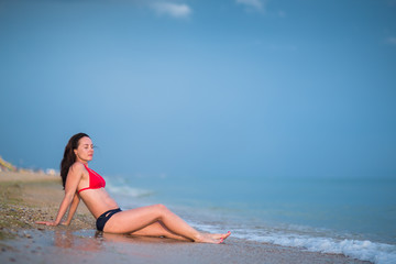 Fototapeta na wymiar portrait of brunette girl with long hair in red bikini in full length sunbathing on sandy beach