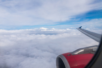 Naklejka na ściany i meble View of the clouds, the wing of the aircraft and the engine of the aircraft from the window of a flying airplane