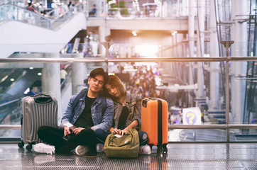 Traveling concept. Happy Asian couple asleep waiting for boarding in airport holding passport with tickets and luggage.