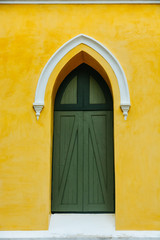 an arched green wooden door decorate with white stucco arch on the top in the yellow fresco plaster cement wall finishing
