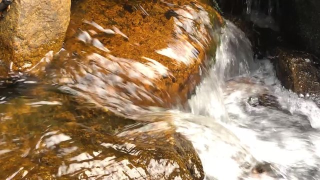 Close up of water cascading down over orange rock in a river