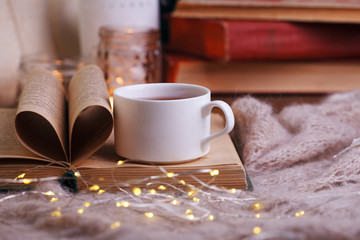 Warm knitted blanket, cup of hot tea and book on a wooden tray, autumn, winter seasonal background, love to read concept, cozy relax time in homely room