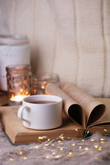 Obraz na płótnie Canvas Warm knitted blanket, cup of hot tea and book on a wooden tray, autumn, winter seasonal background, love to read concept, cozy relax time in homely room