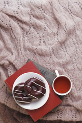 Still life details in home interior of living room. Cup of tea and chocolate donuts on stack of book. Breakfast in autumn and winter morning. Cozy relax seasonal concept.