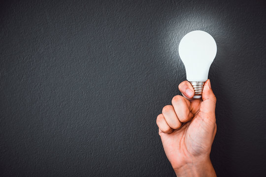 Man's Hand Holding LED Light Bulb  Over Black Color Wall Background With Copy Space, Concept Of Ideas