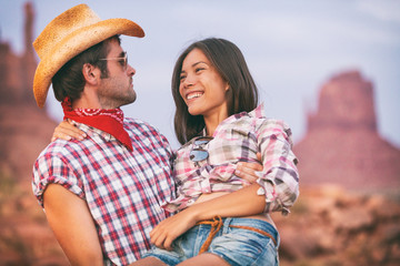 Lovers cowboy and cowgirl in love cute couple in USA backcountry landscape. Boyfriend wearing cowboy hat carrying Asian girlfriend seducing and flirting.