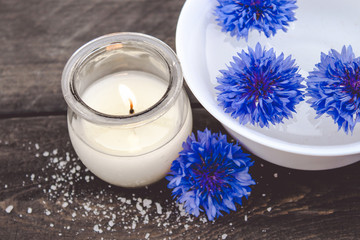 Obraz na płótnie Canvas blue cornflowers lie in the water in a white bowl near a burning candle on the background of old boards.