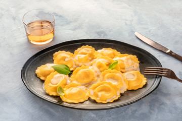 A plate of cooked Italian ravioli garnished with fresh basil leaves, with a glass of white wine and a place for text