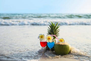 Cocktail glasses with coconut and pineapple on clean sand beach - fruit and drink on sea beach backgroudn concept