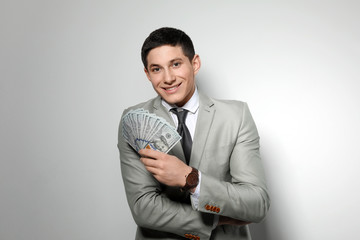 Portrait of young businessman with money fan on light background