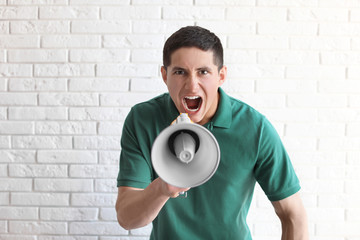 Portrait of young man using megaphone near brick wall