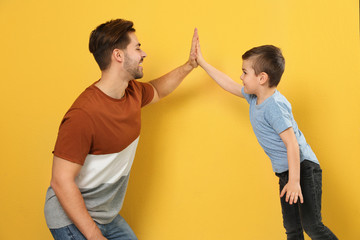 Portrait of dad and his son giving high five on color background