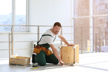 Handyman in uniform assembling furniture indoors. Professional construction tools