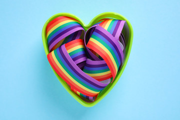 Heart shaped mold with bright rainbow ribbon on color background, top view. Symbol of gay community
