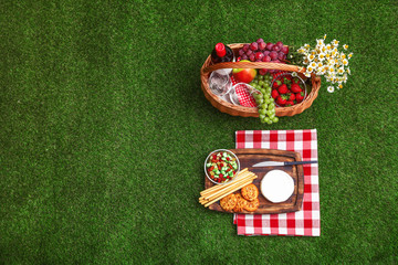 Flat lay composition with picnic basket, wine and products on grass, space for text