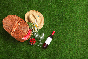 Flat lay composition with picnic basket, wine and strawberries on grass, space for text