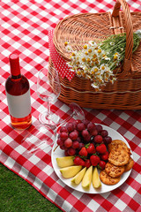 Composition with picnic basket, wine and products on checkered blanket outdoor