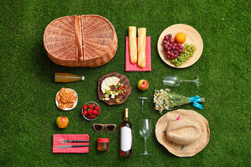 Flat lay composition with picnic basket and products on green grass