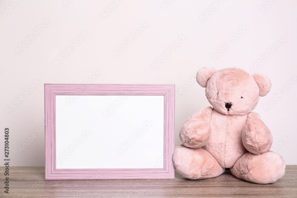 Wall mural photo frame and adorable teddy bear on table against light background, space for text. child room el