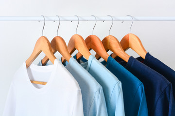 close up collection shade of blue tone color t-shirts hanging on wooden clothes hanger in closet or...