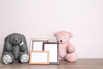 Photo frames and adorable toys on table against light background, space for text. Child room elements