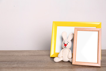 Photo frames and adorable toy bunny on table against light background, space for text. Child room elements
