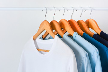 close up collection shade of blue tone color t-shirts hanging on wooden clothes hanger in closet or clothing rack over white background with copy space