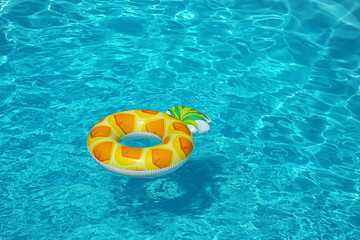 Bright inflatable pineapple ring floating in swimming pool on sunny day. Space for text